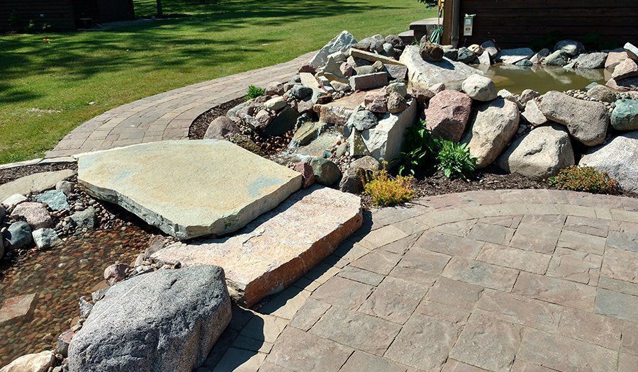 Stone patio with large rocks, pathway, and pond.