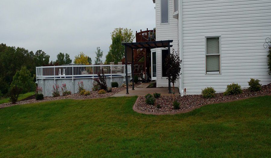 White house with a pool and deck. Green grass in the foreground and a cloudy sky.