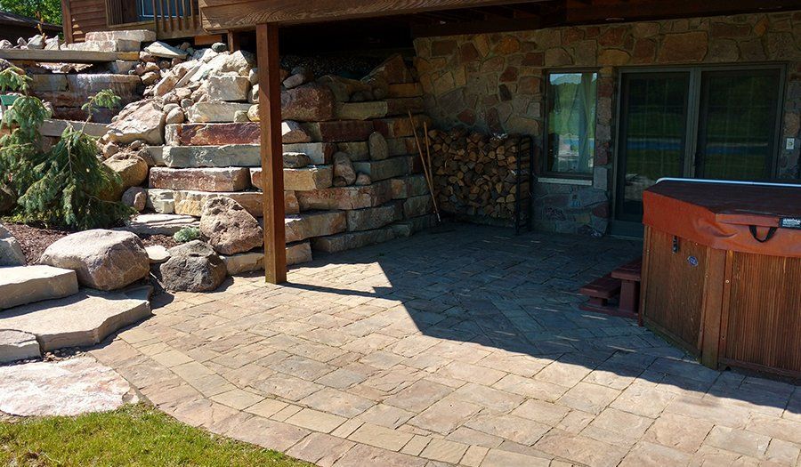 Stone patio with stacked stones, stairs, and a hot tub. Firewood stacked nearby.