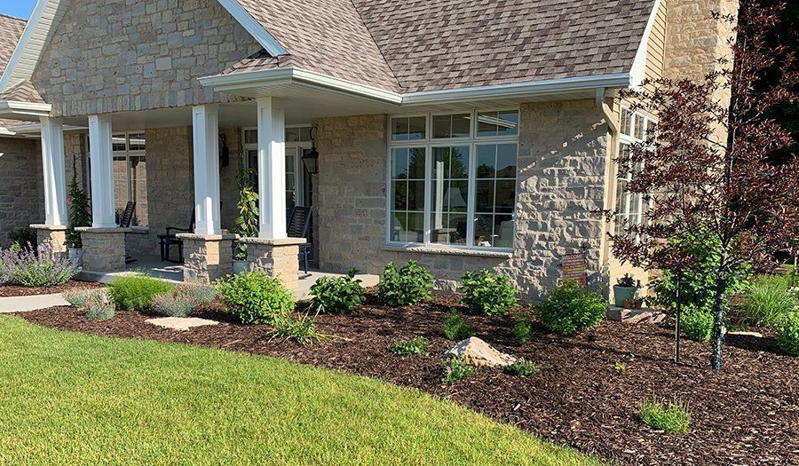 Brick house with a landscaped garden bed filled with plants and mulch, beside a green lawn.