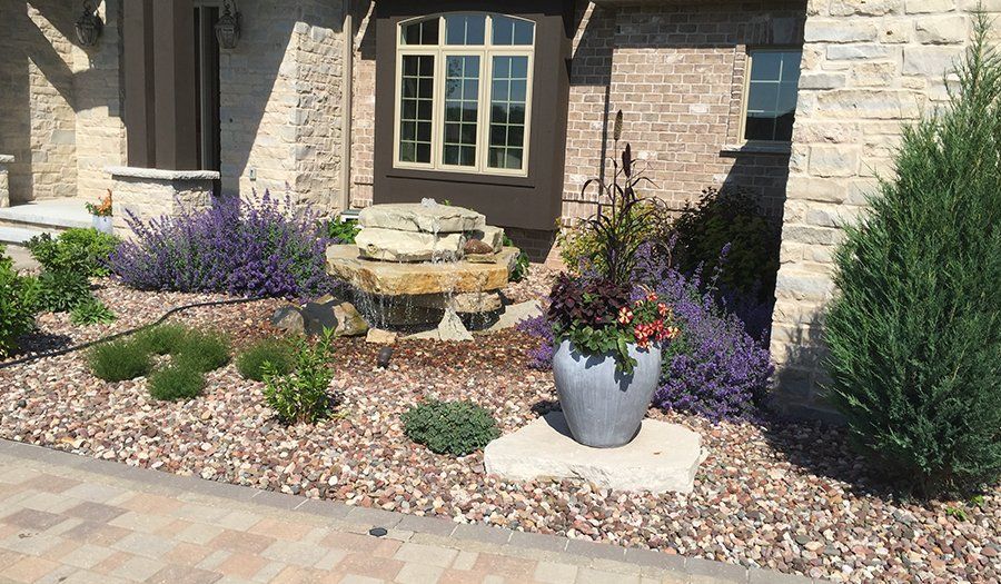 Landscaped front yard with water feature, purple flowers, and potted plants.