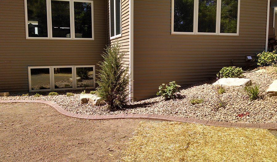 Tan house with windows, surrounded by a gravel landscaping bed with a concrete border, and a patch of dry grass.