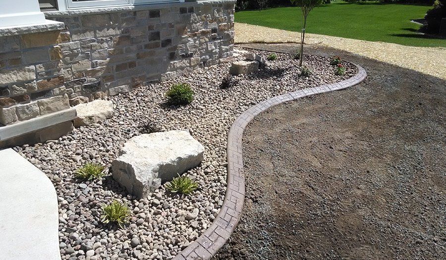 Stone and gravel landscaping with a brick border around a garden bed.