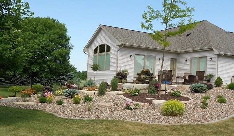 House exterior with landscaped yard, featuring flowers, bushes, and trees on a sunny day.