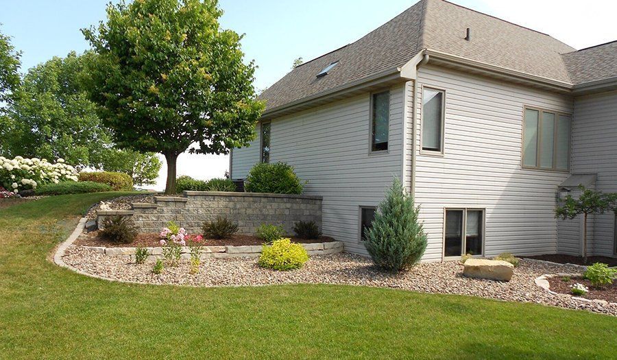 Side view of a house with retaining walls, landscaping, and a green lawn.