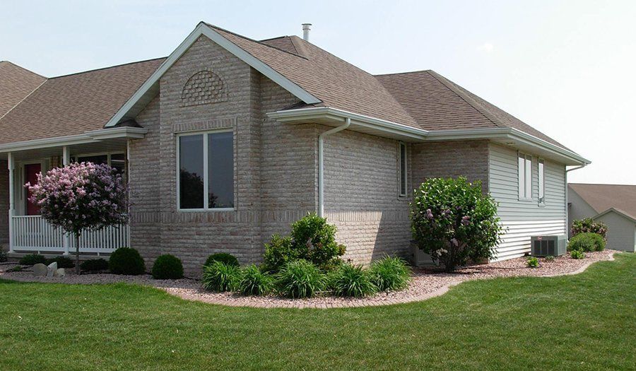 Brick house with brown roof, white trim, and landscaped yard.