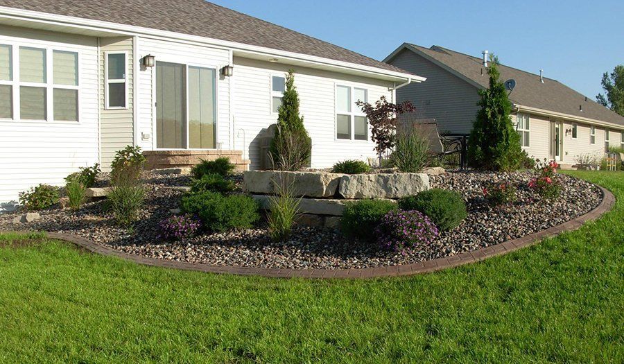 Landscaped backyard with retaining wall, bushes, and decorative stone border.