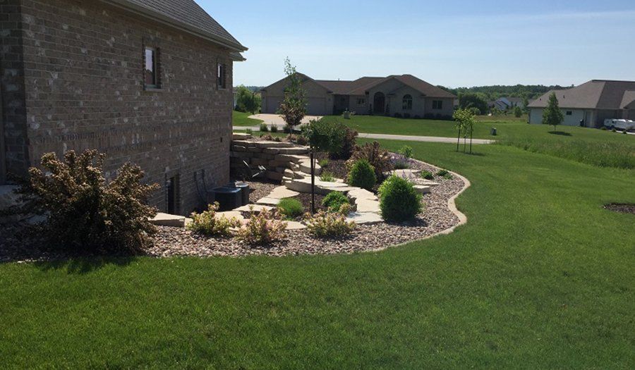 House with landscaped yard, stone edging, lawn, and other houses in background on a sunny day.