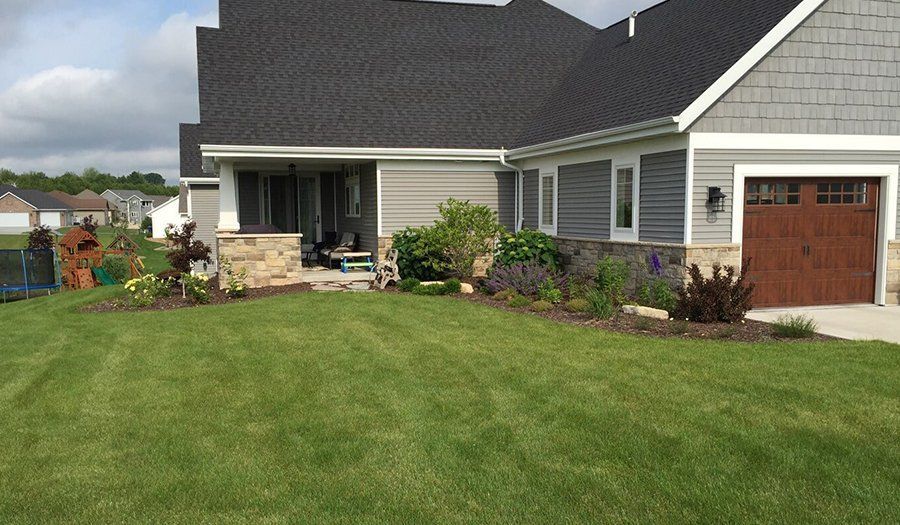 Green lawn with landscaped flower beds in front of a house with a grey roof and garage door.