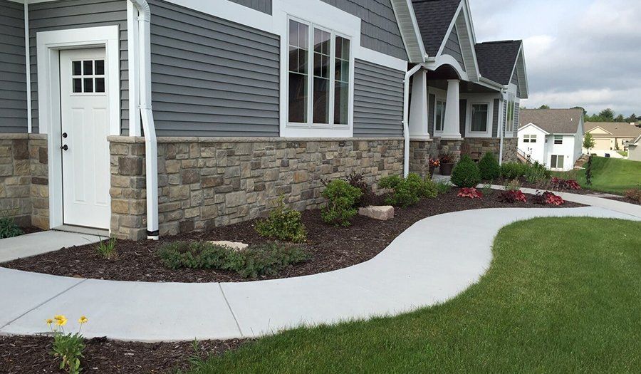 Exterior of house with stone facade, gray siding, white trim, and curved sidewalk.