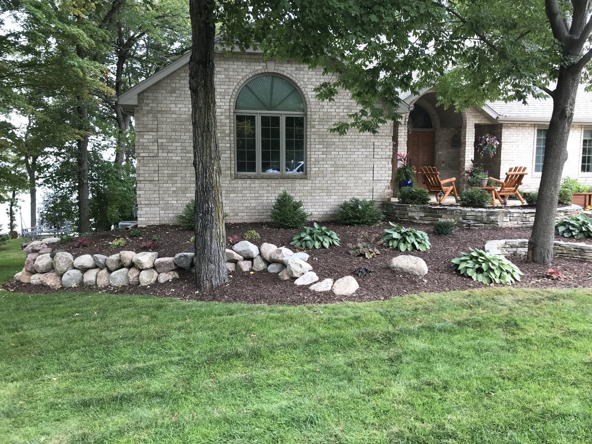 Stone-sided house with a lawn, landscaping, and a semi-circular window, next to trees.