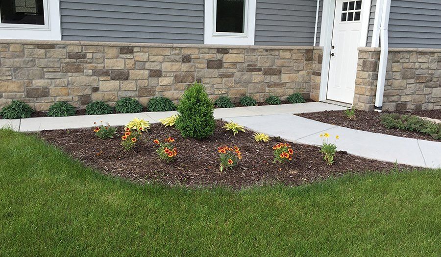 A stone wall with flowerbeds, a walkway, and a green lawn in front of a building.