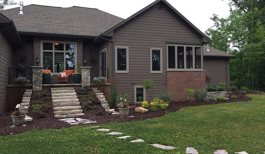 Brown house with stone steps, a lawn, and a path leading towards the entrance.