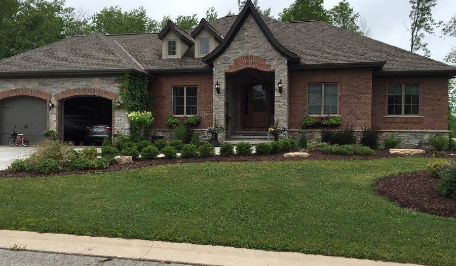 Brick house with garage, arched entry, brown roof, and green lawn.