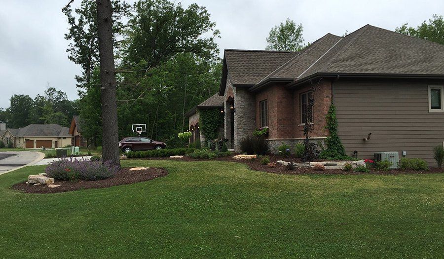 House with brown shingles, brick, and siding, surrounded by green lawn and trees.