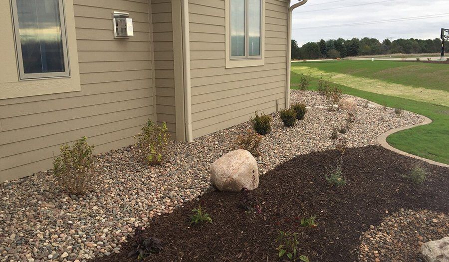 Exterior view of a house with beige siding, rock landscaping, and a grassy lawn.