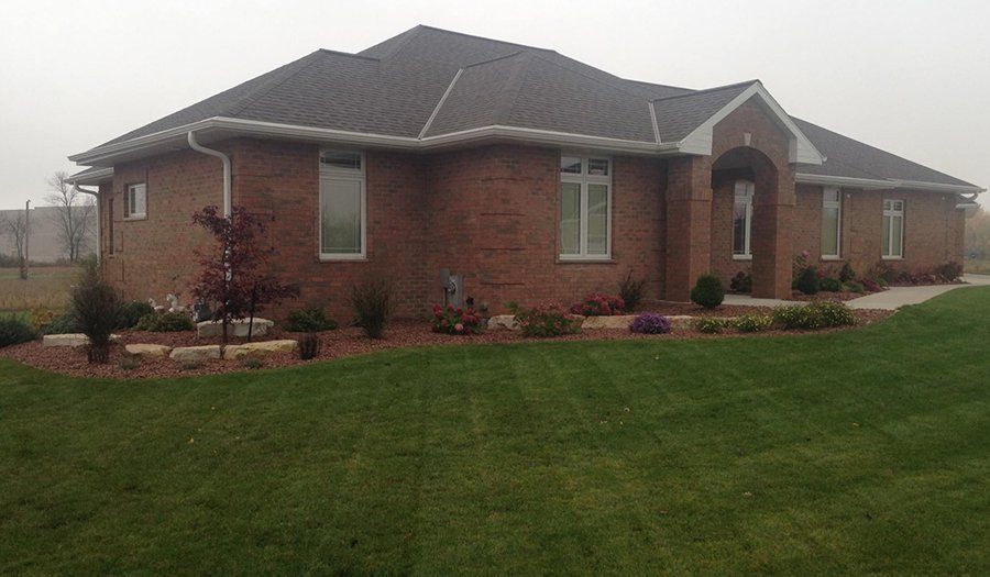 Brick house with brown roof, white trim, and well-manicured lawn.