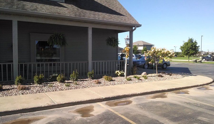 Exterior of building with porch, small plants in front, parked car, clear sky.