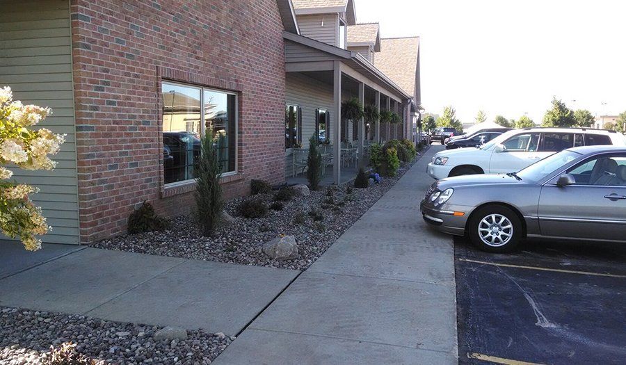 Sidewalk next to a building with a brick wall and parked cars.
