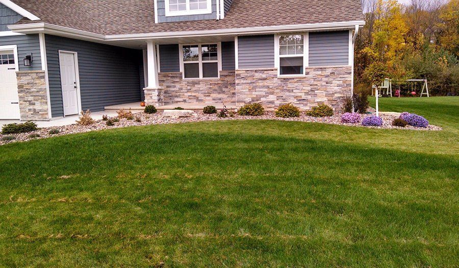 House exterior with blue siding, stone facade, and green lawn. Landscaping with purple flowers.