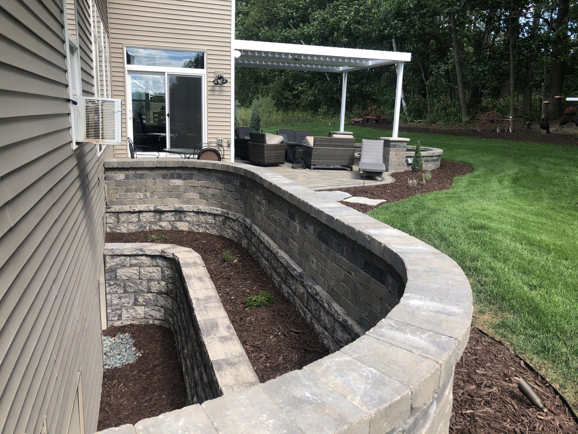 A partially below-ground patio with stone retaining walls, a pergola, and a sliding glass door.