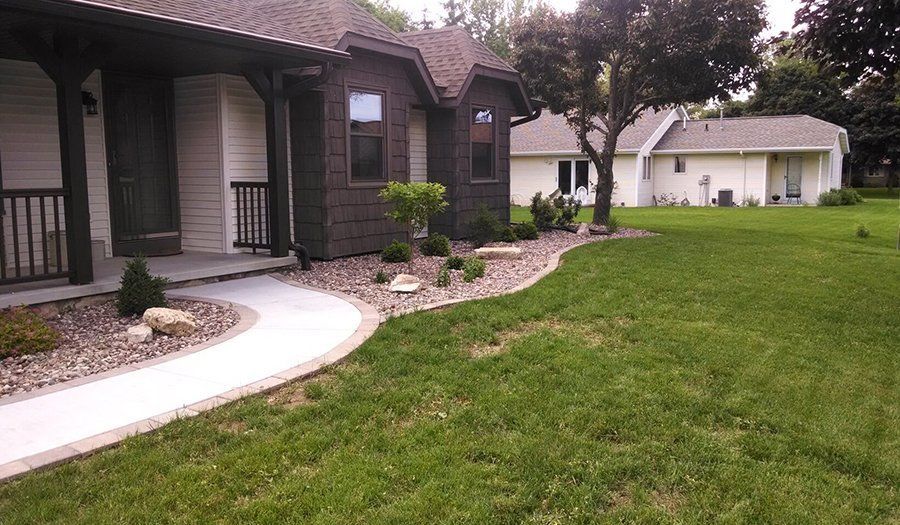 House with dark brown trim, stone walkway, and green lawn. Another house is in the background.