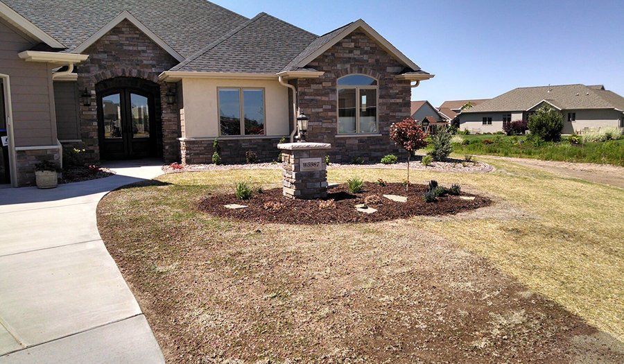 Stone facade house with dark roof and brown landscaping. Gravel driveway.