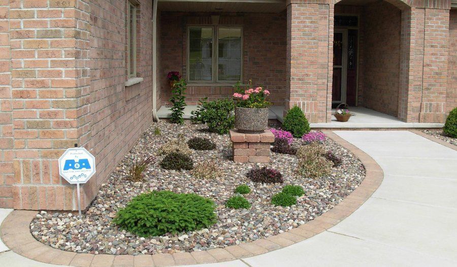 Brick house exterior with a landscaped rock garden. Pink and green plants with a concrete walkway.