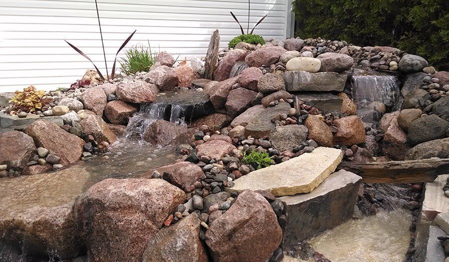 Water flows down a rocky waterfall feature in a garden, surrounded by plants and stones.