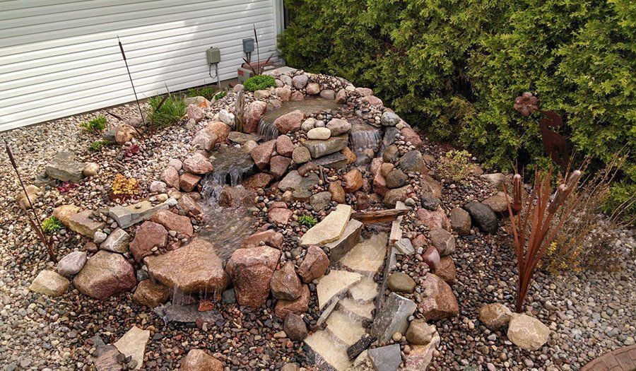 Small rock waterfall feature in a garden, with water flowing over rocks.