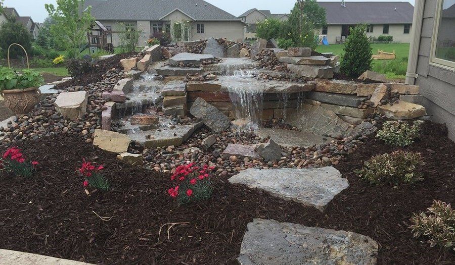 Backyard waterfall with stone tiers and surrounding landscaping.