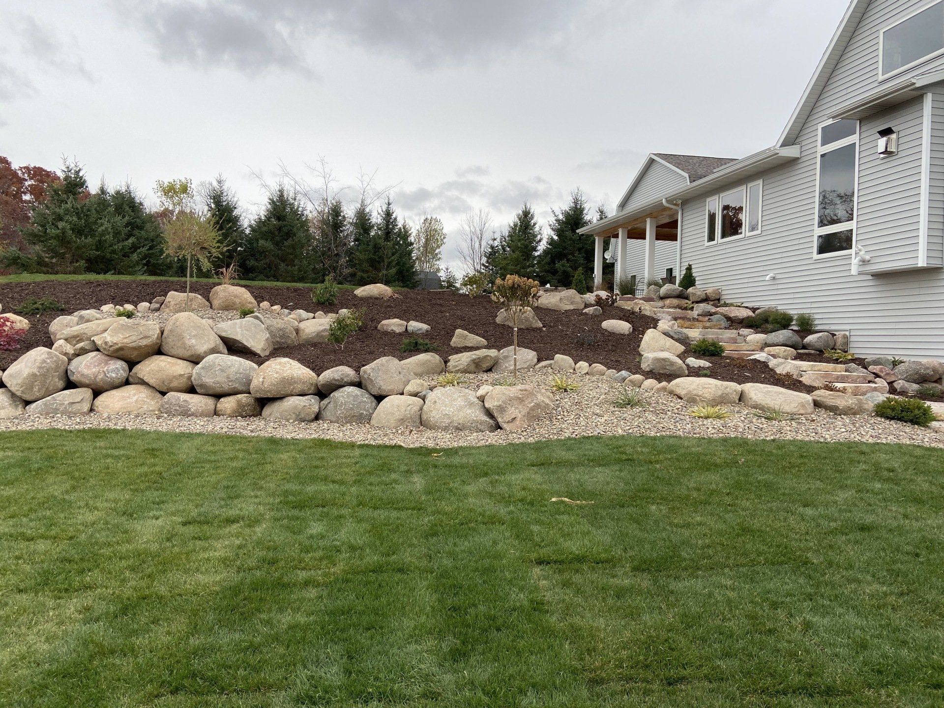 Rock retaining wall in a yard, with a house in the background and a green lawn in the foreground.