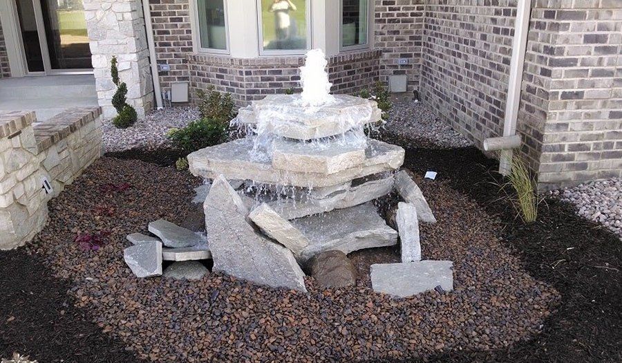 Stone fountain cascading water, surrounded by brown mulch and brick exterior.