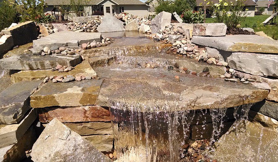 Water cascading over layered, flat rocks in a tiered waterfall feature.