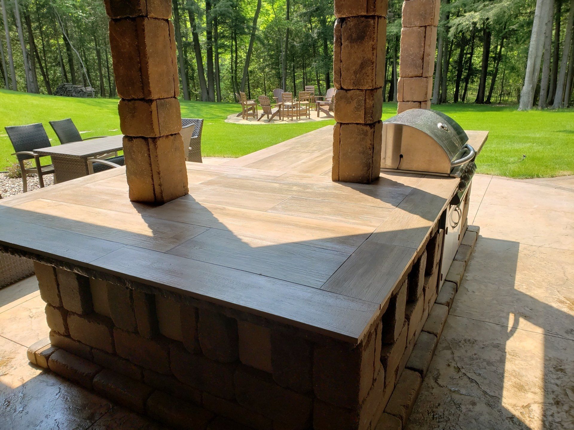 Outdoor brick barbecue island with a concrete countertop. Includes a grill, built in under a covered patio.