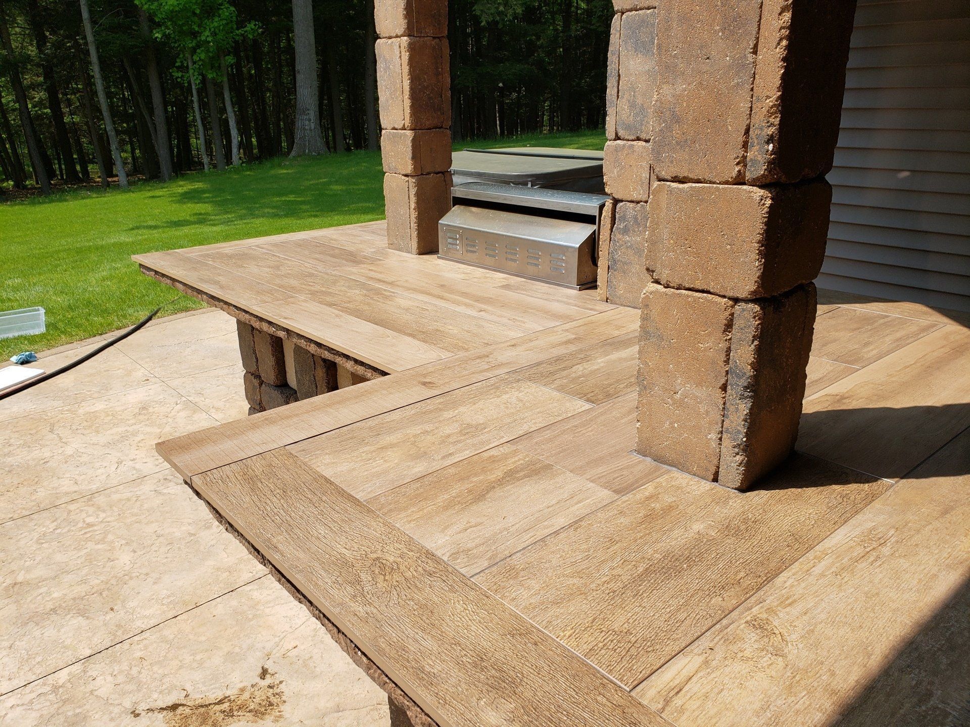 Outdoor patio with brown brick columns and wood-like flooring. A small waterfall is visible in the background.