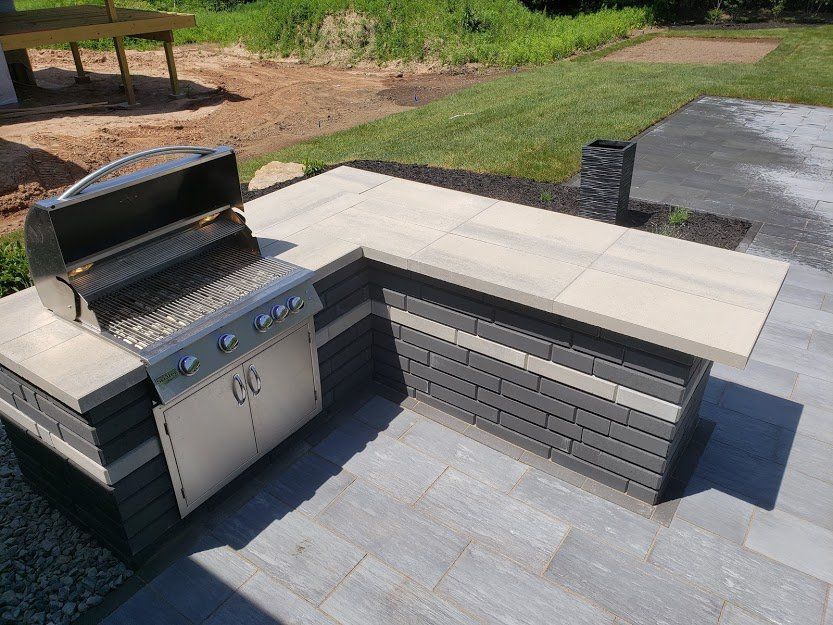 Outdoor grilling station with stainless steel grill, gray brick and concrete countertop.