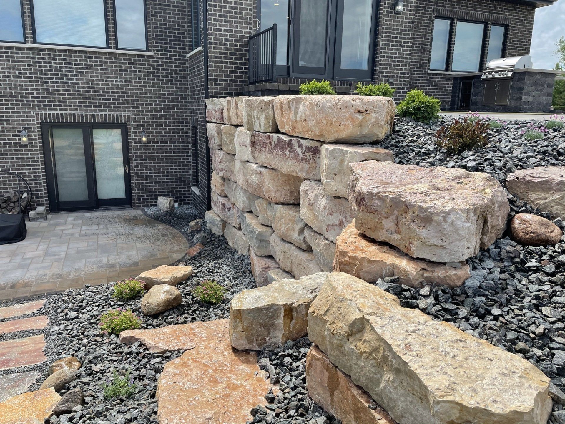 Stone retaining wall with a brick house and landscaped yard.