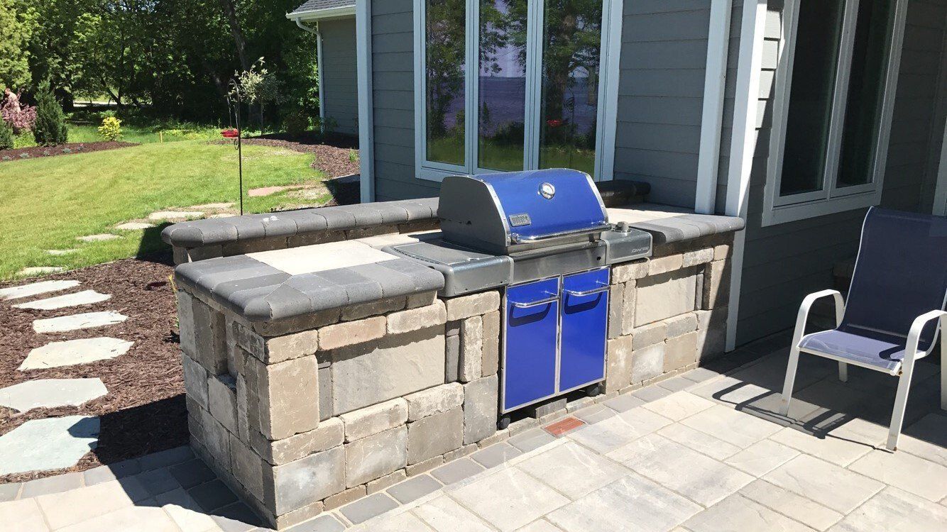 Outdoor grilling station with blue grill, built-in to a stone structure on a patio.