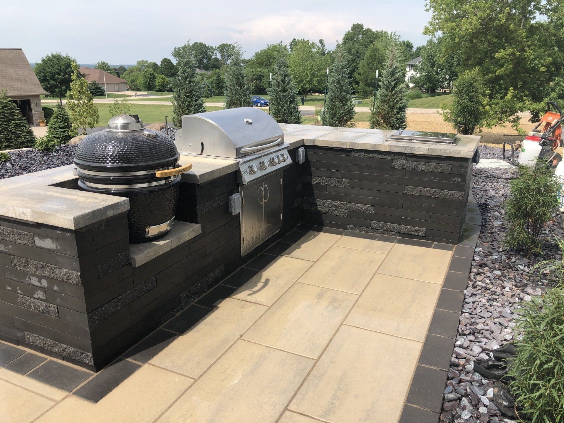 Outdoor kitchen with black brick, stainless steel grill, and charcoal smoker on a patio.