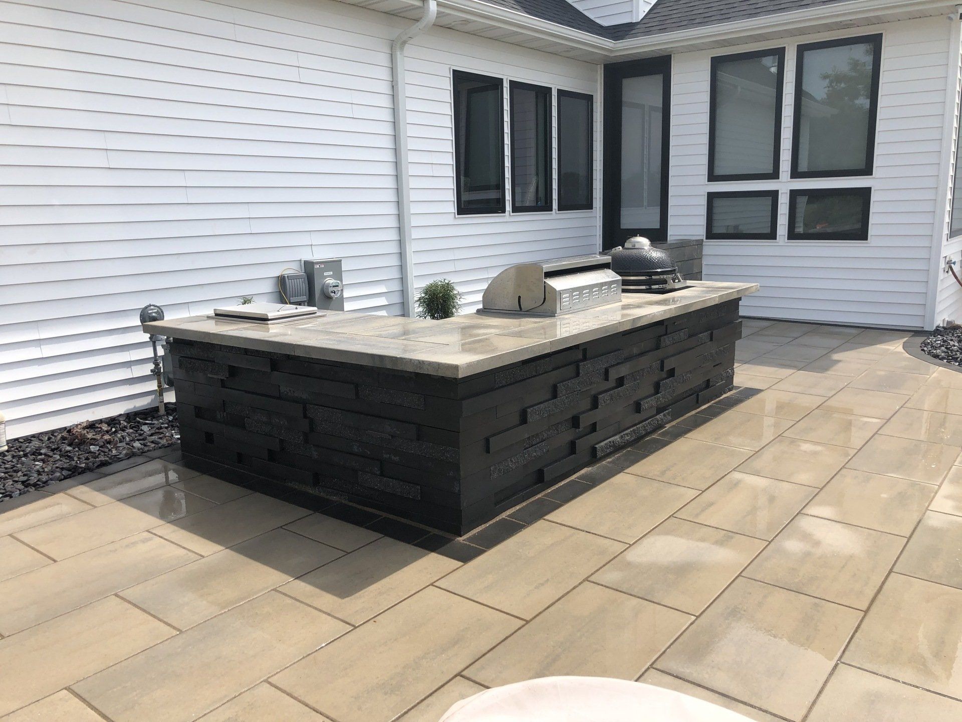 Outdoor kitchen with black stone facade, concrete countertop, and grill, on patio.