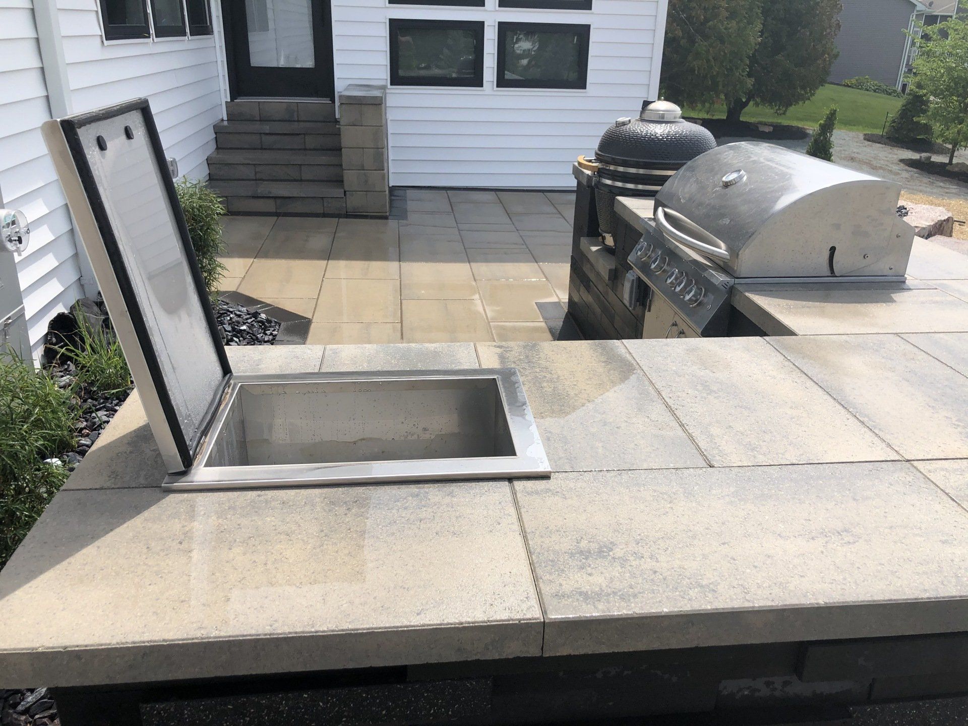 Outdoor kitchen with a built-in cooler and grill on a stone patio.
