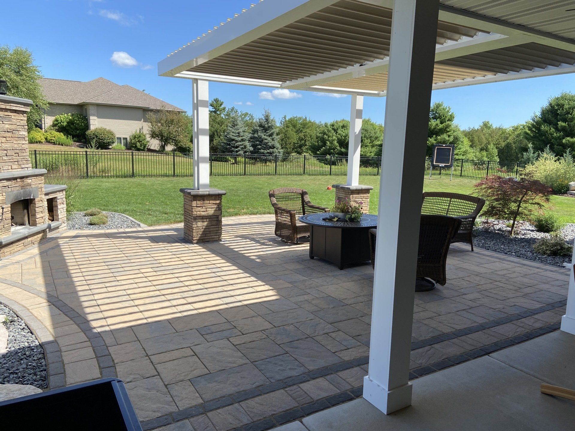 Patio with pergola, stone fireplace, and seating area overlooking a grassy backyard.
