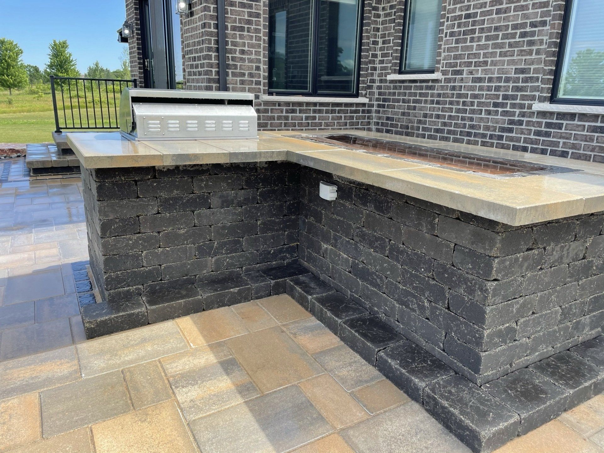 Outdoor kitchen with a grill and fire pit, built of dark gray brick, with a stone countertop.