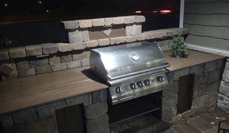 Outdoor built-in grill with stainless steel hood on a stone counter, flanked by storage compartments.