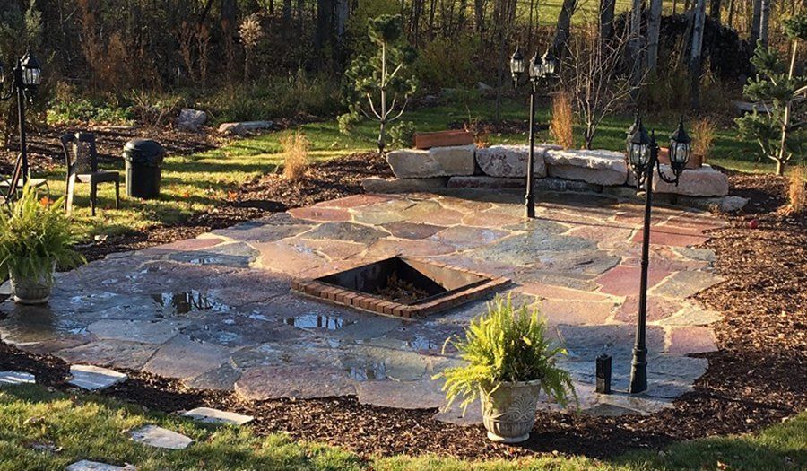 Fire pit patio with flagstones, surrounded by mulch, plants, and lampposts, set in a yard.