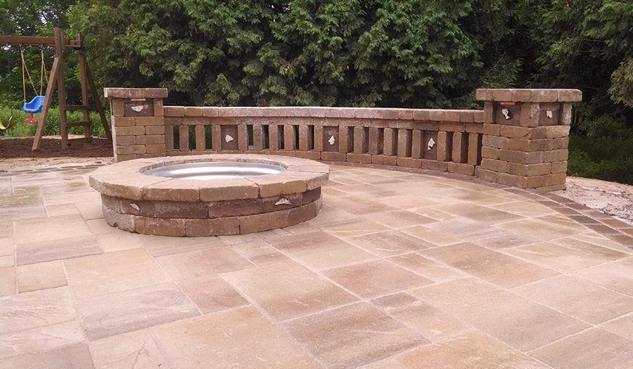 Stone patio with fire pit and decorative wall in a backyard.