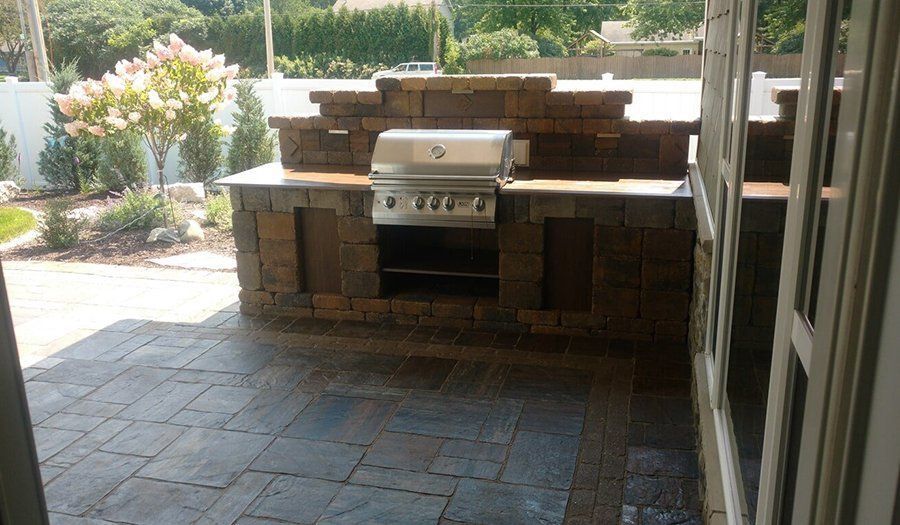 Outdoor kitchen with built-in grill on a stone patio.