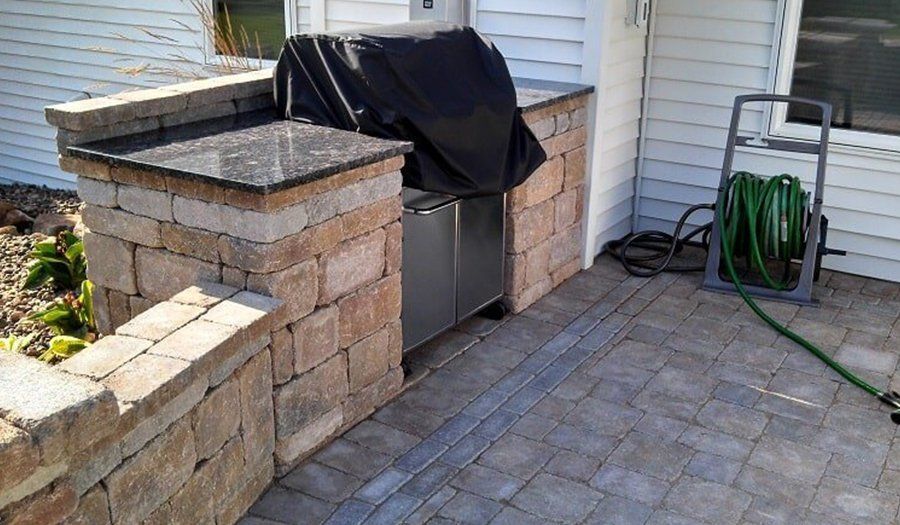 Outdoor kitchen with stone walls, granite countertops, grill covered, and hose reel.
