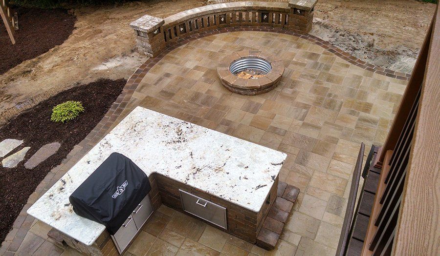 Patio with stone pavers, outdoor kitchen, fire pit, and curved seating wall.